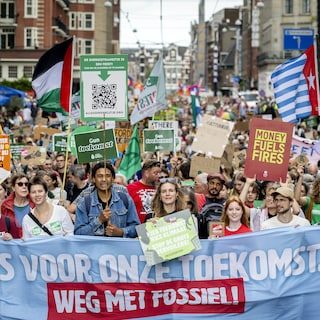 Tienduizenden demonstranten trekken door binnenstad Amsterdam voor klimaatmars, deelnemers dragen borden over hittereco…
